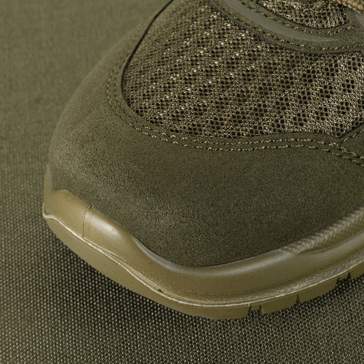 Lähikuva M-Tac Tactical Sneakers IVA:sta hengittävällä meshillä ja vahvistetulla kärjellä, otettu vihreällä taustalla.