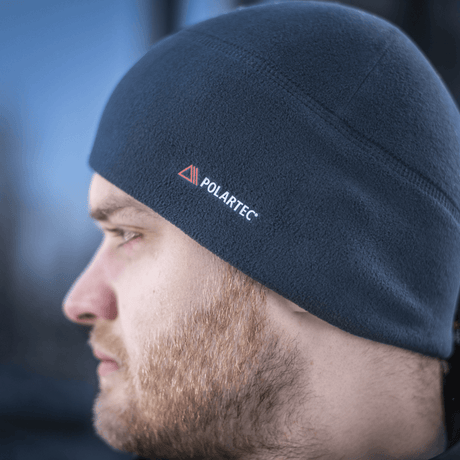 Mies pukeutuneena M-Tac Fleece Watch Cap Light Polartec, näyttää pehmeän ja lämpimän talvihatun Polartec-logolla, sopii kylmään ja tuuleen.