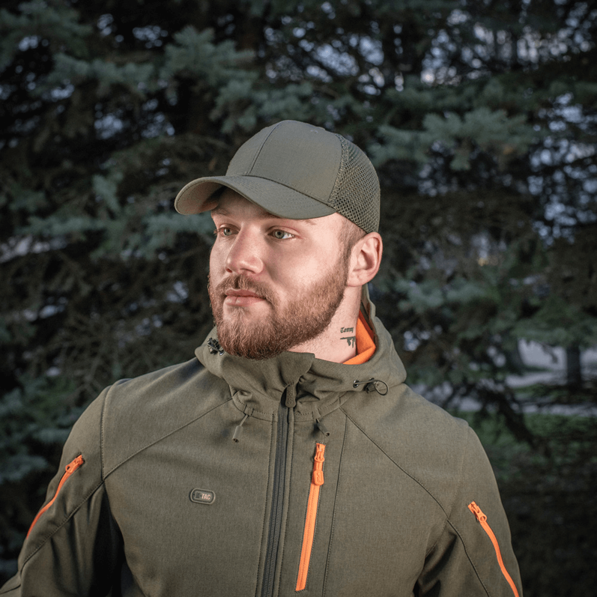 M-Tac Mesh Flex Ripstop Baseball Cap vihreänä, henkilö käyttää sitä armeijaa muistuttavassa takissa metsäalueella.