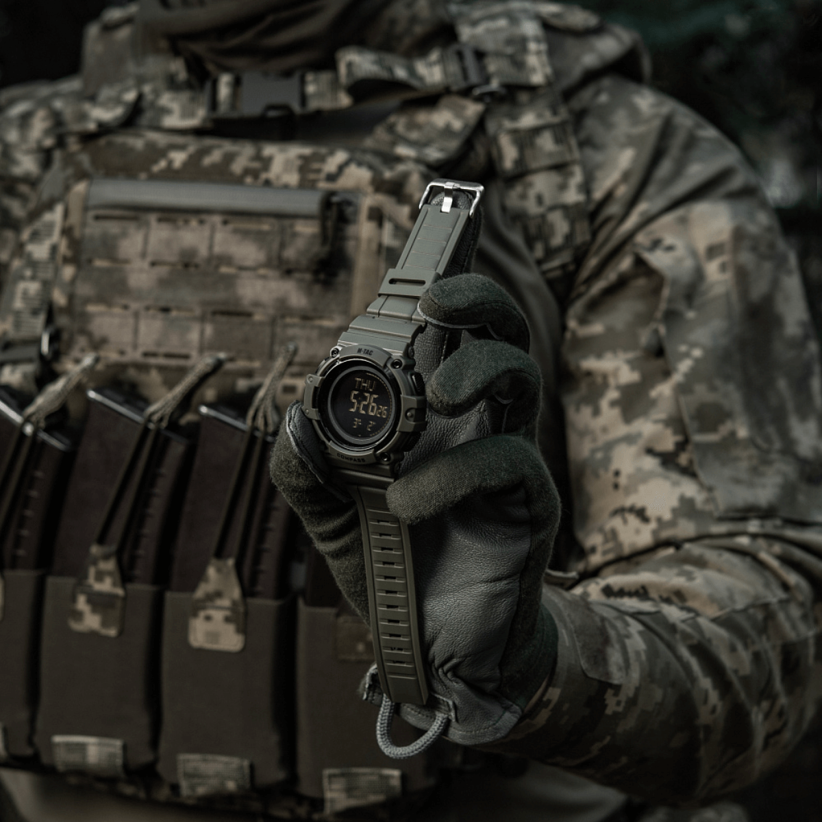 M-Tac Tactical Ur med Kompas 2233 pidetty taktisesti pukeutuneen henkilön toimesta, näyttää kestävän kellomuotoilun ulko- ja arkeen.