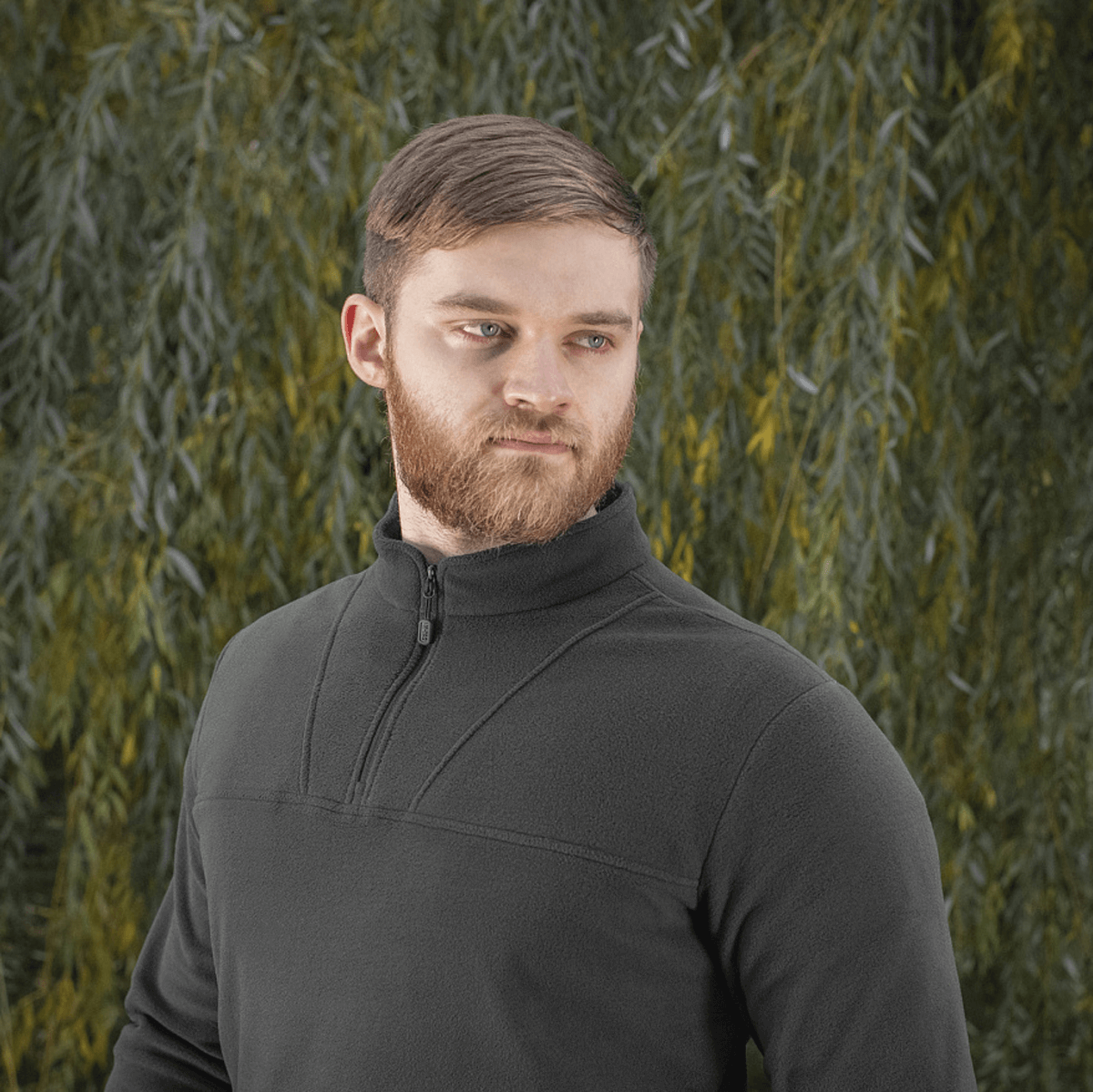 Mies pukeutuneena M-Tac Delta Polartec fleece-takkiin vihreän taustan edessä.