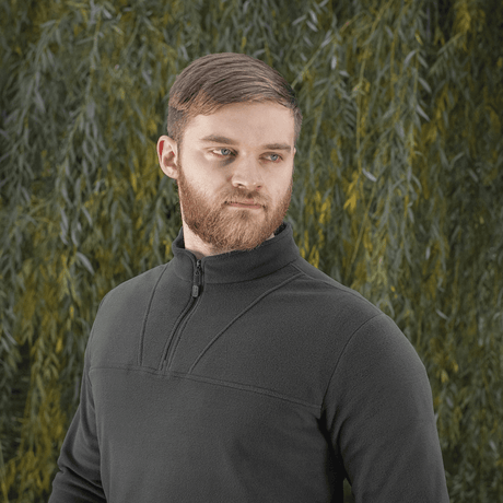 Mies pukeutuneena M-Tac Delta Polartec fleece-takkiin vihreän taustan edessä.