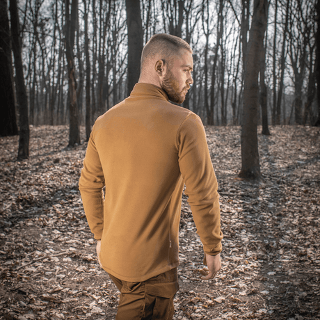 Mies pukeutuneena M-Tac Delta Polartec fleece-takkiin metsässä nähtynä takaa, näyttää tyylin ja toiminnallisuuden luonnoympäristössä.