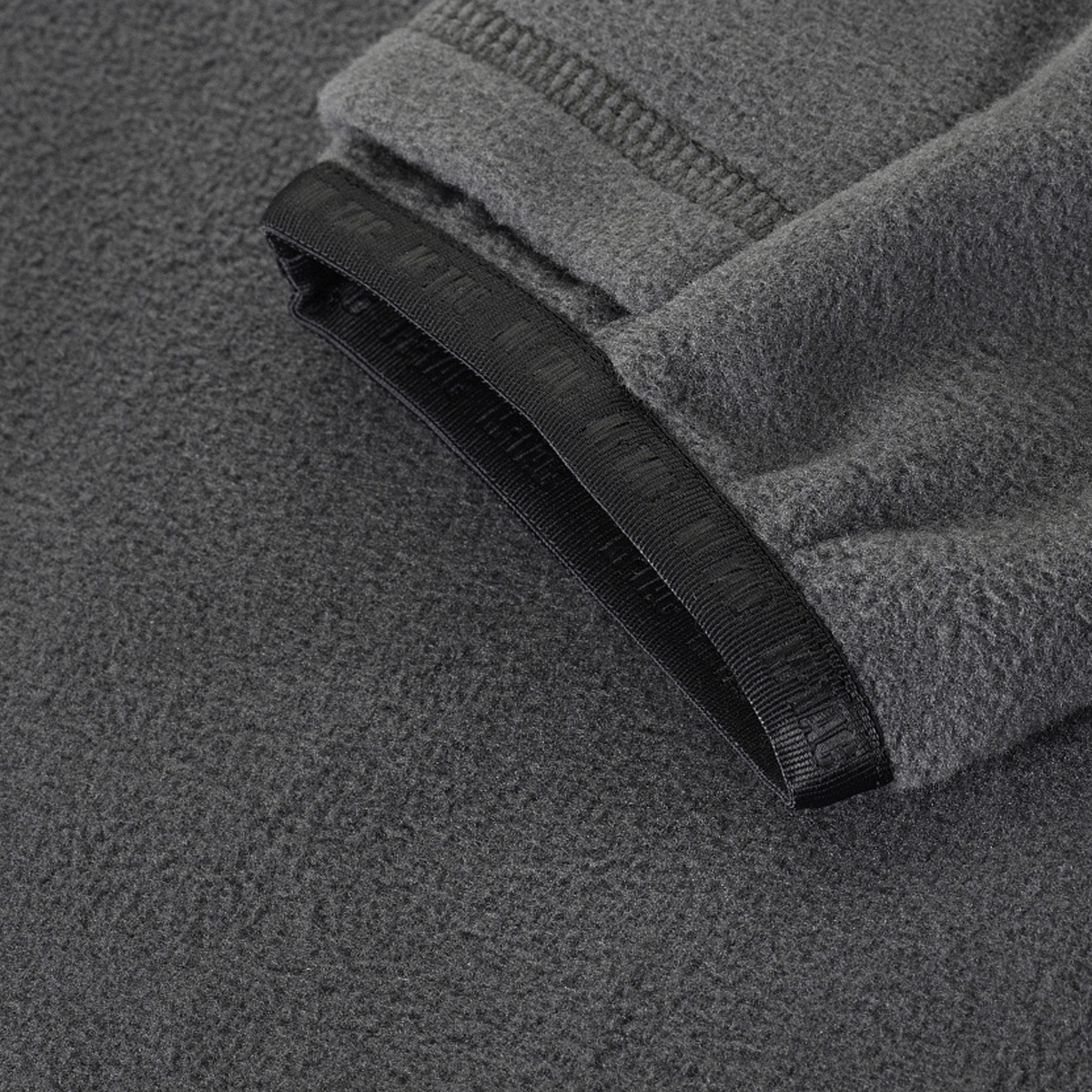 Lähikuva M-Tac Delta Polartec -fleece-takin kangasdetailista harmaana, korostaen rakennetta ja reunoja.