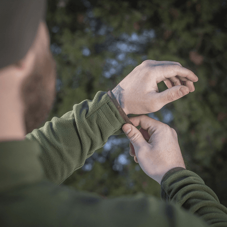 Mies säätää hihansuutta M-Tac Delta Polartec fleece-takissa metsässä, näyttää takin toiminnallisen suunnittelun ja materiaalin.