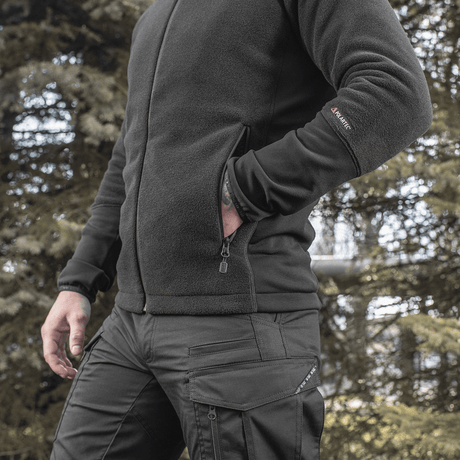 Mies pukeutuneena M-Tac Polartec Sport -fleecatakkiin metsässä, toimii lämpimänä ja toiminnallisena välikerroksena viileään säähän.