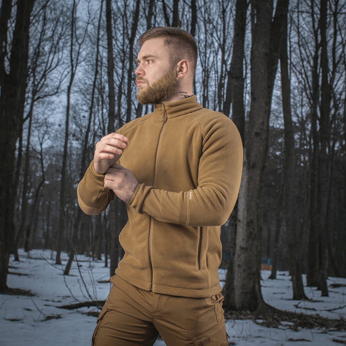 Mies, jolla on M-Tac Polartec Sport Fleecejakke, seisoo lumisessa metsässä ja esittelee takin mukavuutta ja toimivuutta kylmässä säässä