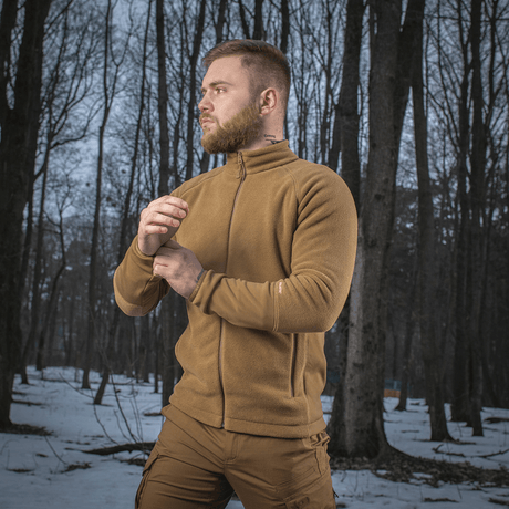 Mies, jolla on M-Tac Polartec Sport Fleecejakke, seisoo lumisessa metsässä ja esittelee takin mukavuutta ja toimivuutta kylmässä säässä