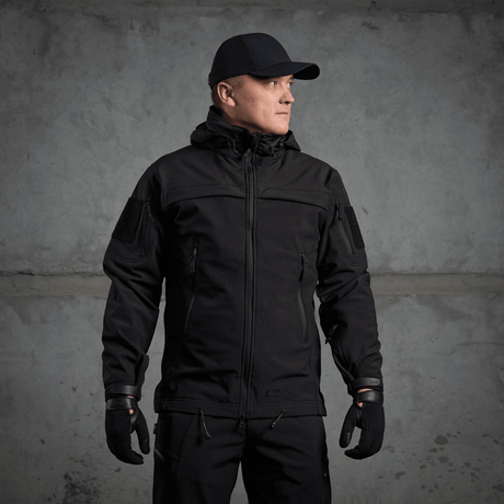 Mies pukeutuneena M-Tac Soft Shell Police Jakkeen, musta takki säädettävin yksityiskohdin ja sisäinen fleece, suunniteltu tuulta ja säätä vastaan.