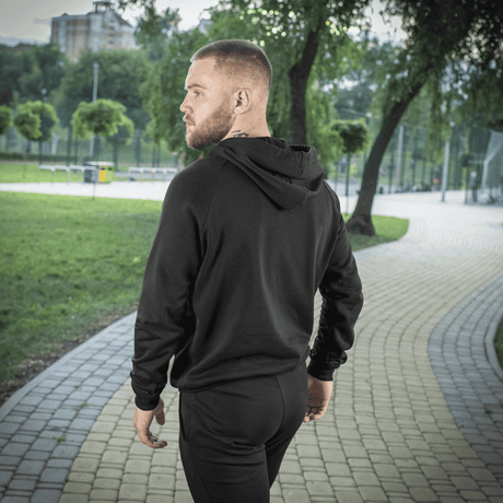 Mies M-Tac Cotton Raglan -hupparissa kävelemässä puistossa, korostaa mukavuutta ja tyyliä.