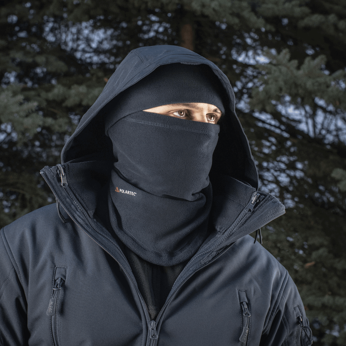 Mies käyttää M-Tac Anatominen Tube Scarf Polartec-nyörillä kasvomaskina metsäympäristössä. Polartec-fleece tarjoaa lämpöä ja suojaa.