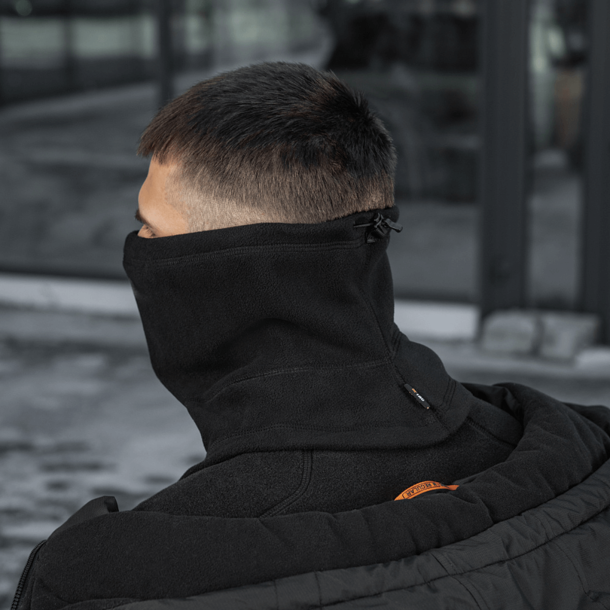 Mies käyttää M-Tac Anatomisk Snood Justerbar Elite Fleece (320 g/m²) kaulalämmittimenä, säätö näkyvissä takana, suojaa elementtejä vastaan.