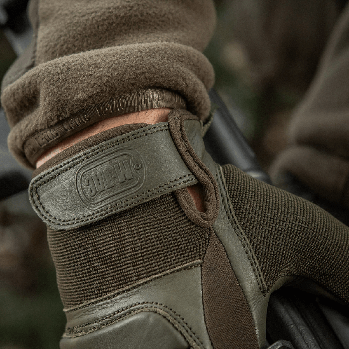 M-Tac Assault Tactical Mk.2 -hanskat käytössä, säädettävä velcro-ranne ja synteettinen paneeli paremman otteen saamiseksi.