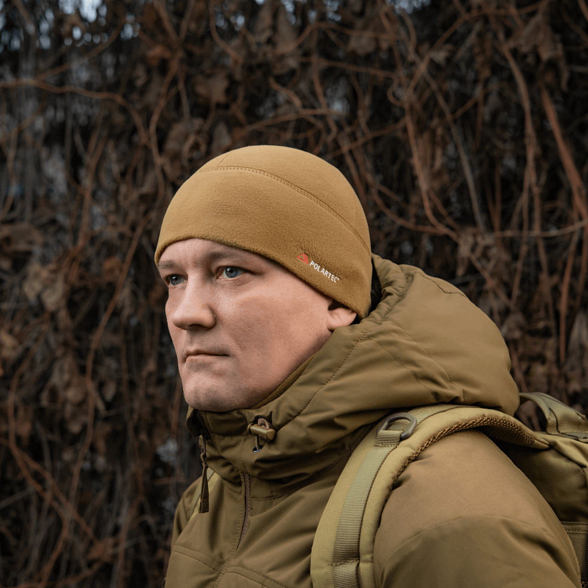 Mies pukeutuneena M-Tac Fleece Watch Cap Light Polartec hattuun ruskeissa sävyissä, sopii suojaksi kylmältä ja tuulelta.