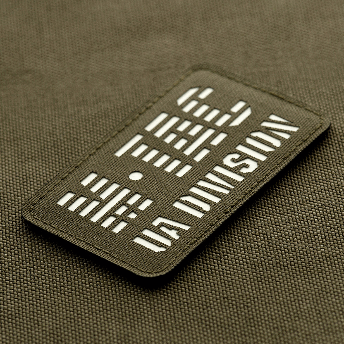 M-Tac Patch UA Division Laser Cut pimeässä hohtavalla materiaalilla, kiinnitetty Velcrolla Cordura 500D -pintaan. Koko: 80x50 mm.