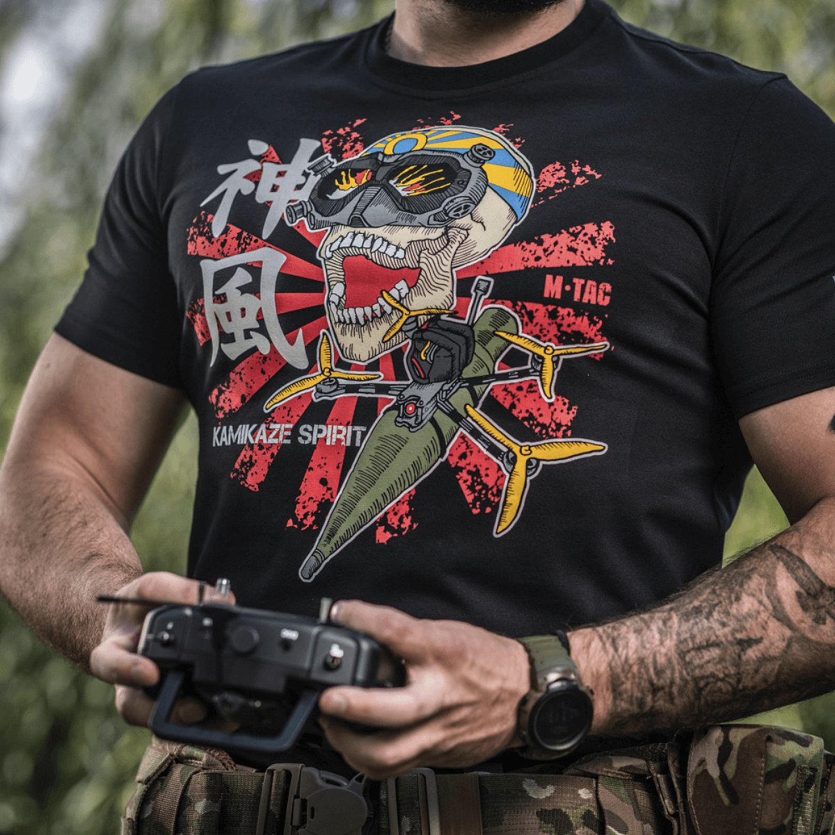 Mies M-Tac T-Shirt Kamikaze Spirit -paidassa FPV-kuviolla pitelee drone-ohjainta; musta T-Shirt, tyylitelty kalloprintti.