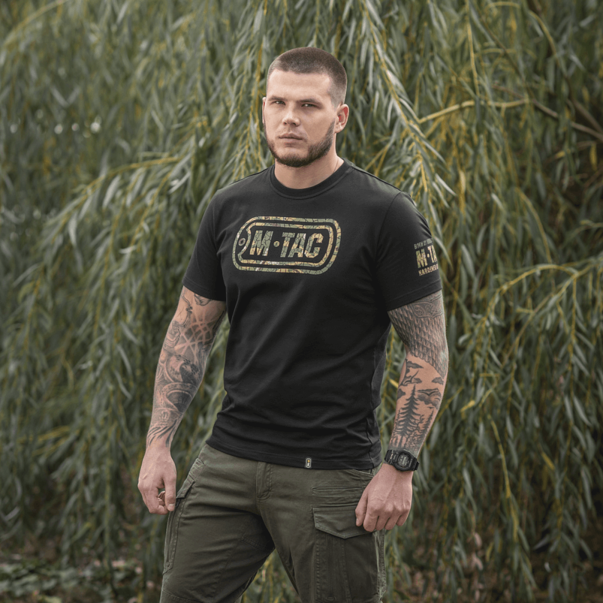 Mies M-Tac T-Shirt Logo -paidassa, camo-kuvio ja sloganit luonnossa.