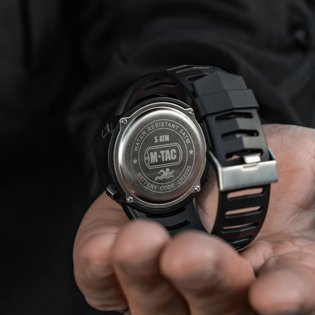 M-Tac Tactical kello 2147 kädessä, takakannessa tekstit 'WATER RESISTANT 5ATM' ja 'BATTERY CODE CR2032', 5atm, cr2032 en