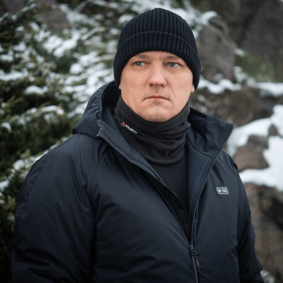 Mies käyttää M-Tac Tube Scarf Polartec -kauluria talvimaisemassa, lämmin ja tyylikäs ulkoiluun.