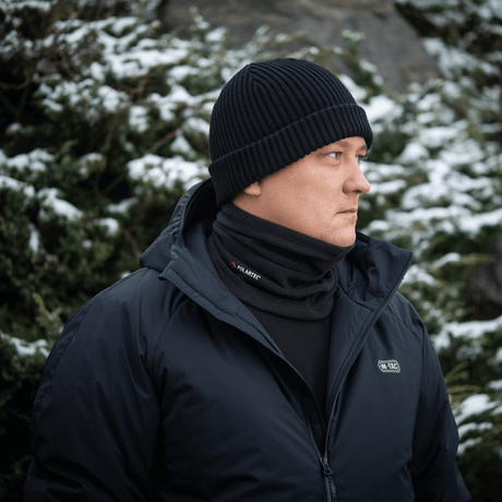 Mies pukeutuneena M-Tac Tube Scarf Polartec -kauluriin lumipeitteisten kuusten edessä; lämmin monitoiminen kauluri talvikäyttöön.