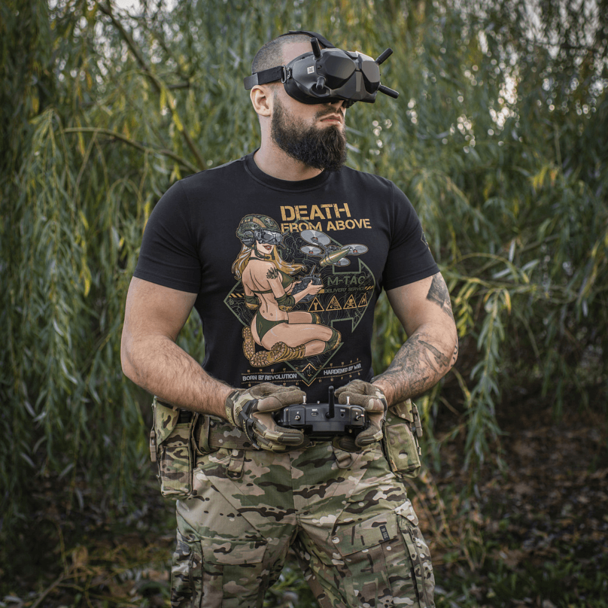 Mies pukeutuneena M-Tac T-Shirt Delivery Service -paitaan Pin-up-printillä ja drone-laseilla, musta paita 'Death from Above' -tekstillä metsäympäristössä.