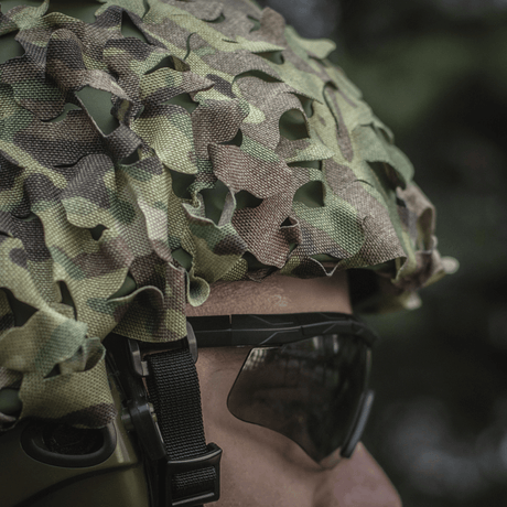 M‑Tac Vilha Hjelmcover Elite Multicam-camossa henkilöllä, valmiina suojaamaan kypärää likaa ja kulumista vastaan haastavissa olosuhteissa.