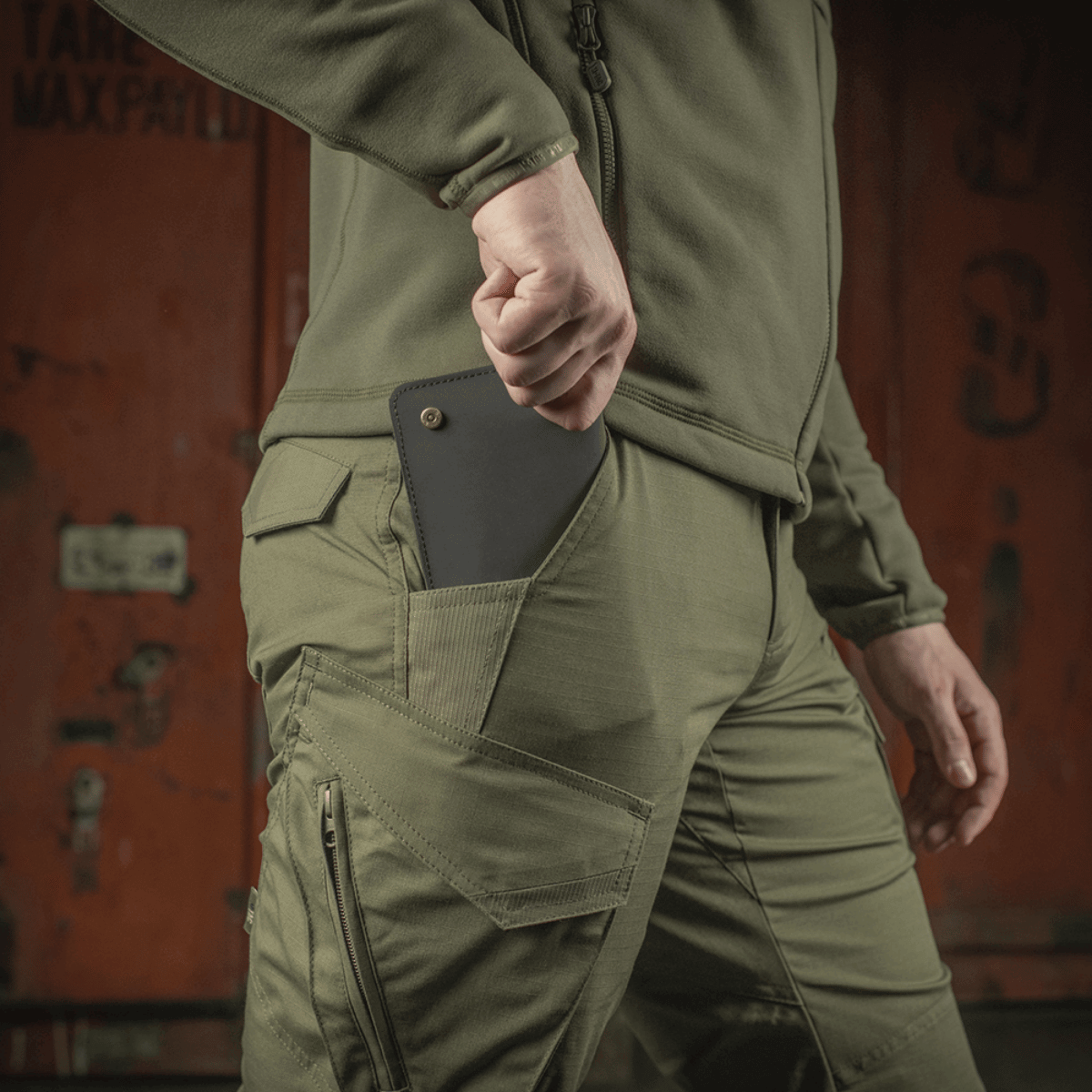 M-Tac Aggressor Gen. II Flex oliivinvärisenä, tasku ja puhelin ulkoilua varten.