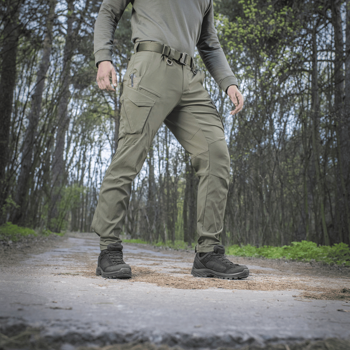 Henkilö pukeutuneena M-Tac-housuihin Aggressor Summer Flex metsässä, kevyet rip-stop-nylonkankaat, sopii kuumaan säähän ja ulkoiluun.