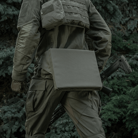 Henkilö taktisessa varustuksessa M-Tac-istuinalustan vyön kanssa metsäympäristössä.