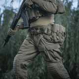 Henkilö pukeutuneena M-Tac War Belt ARMORiin ja taktiikka-varusteisiin luonnossa, valmis taistelutehtäviin.