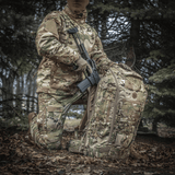 M-Tac Rygsæk Large Gen.III Elite camouflagedesign yhdessä taktisen varustuksen kanssa metsäympäristössä.