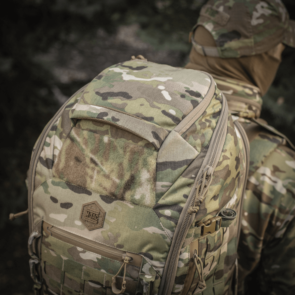 M-Tac Rygsæk Large Gen.III Elite camouflagemallissa, kantaja pukeutuneena sotilasvarusteisiin metsäalueella.