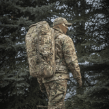 M-Tac Rygsæk Large Gen.III Elite taktiseen käyttöön, henkilö kantaa sitä camouflagessa varustuksessa ulkona metsässä.