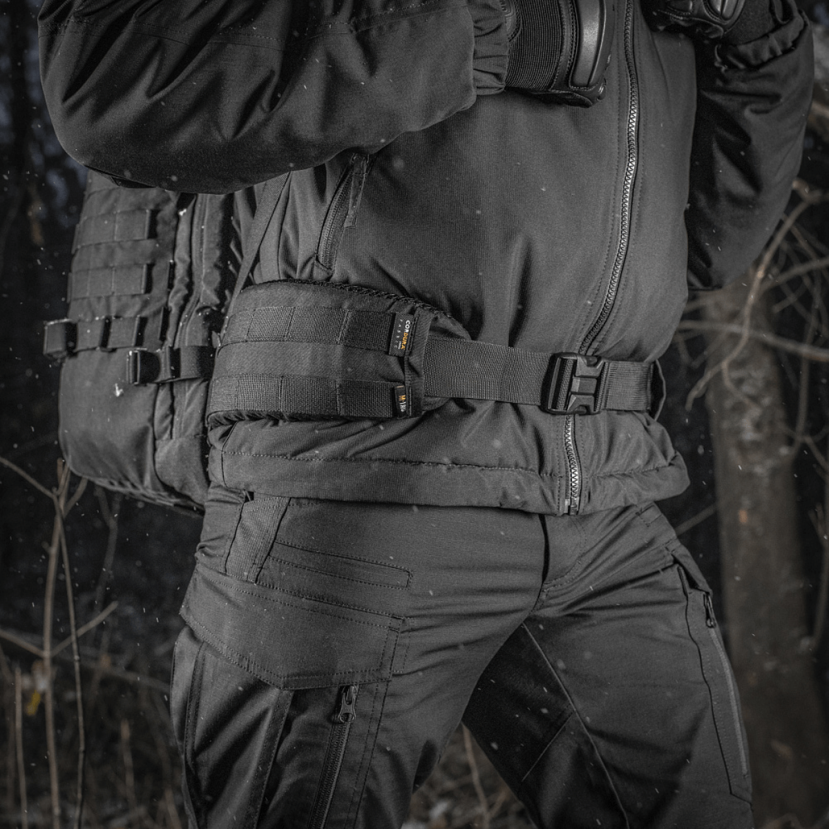 M-Tac Rygsæk Gen.II Elite Large kantajana henkilö talvivaatteissa metsässä, valmistettu kestävästä Cordura-materiaalista maksimaalista kestävyyttä varten.
