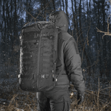 Henkilö kantaa M-Tac Rygsæk Gen.II Elite Largea talvisessa metsässä, lumisateen ympäröimänä.