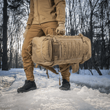 M-Tac Rygsæk Gen.II Elite Large, henkilö kantaa reppua lumisessa metsässä, valmistettu kestävästä Cordura-materiaalista ja siistillä muotoilulla.