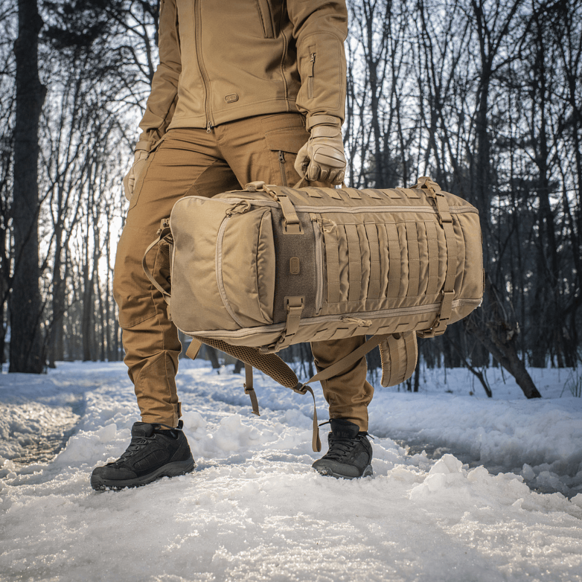 M-Tac Rygsæk Gen.II Elite Large, henkilö kantaa reppua lumisessa metsässä, valmistettu kestävästä Cordura-materiaalista ja siistillä muotoilulla.