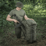 M-Tac Rygsæk Gen.II Elite Large, metsässä aseiden kanssa; näyttää kestävän rakenteen ja toiminnallisuuden ulkoiluseikkailuihin.