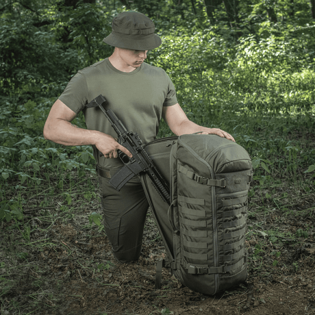 M-Tac Rygsæk Gen.II Elite Large, metsässä aseiden kanssa; näyttää kestävän rakenteen ja toiminnallisuuden ulkoiluseikkailuihin.