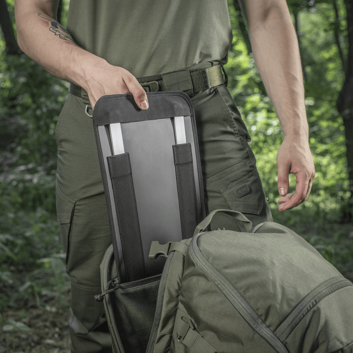 M-Tac Rygsæk Gen.II Elite Large, henkilö ottaa jotain repusta metsäympäristössä.