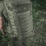 M-Tac Rygsæk Gen.II Elite Large, henkilö luonnossa; repun kestävä Cordura-muotoilu ja tilavat säilytysmahdollisuudet näkyvät.