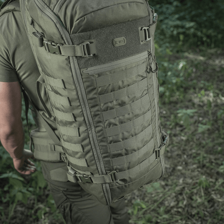 M-Tac Rygsæk Gen.II Elite Large, henkilö luonnossa; repun kestävä Cordura-muotoilu ja tilavat säilytysmahdollisuudet näkyvät.