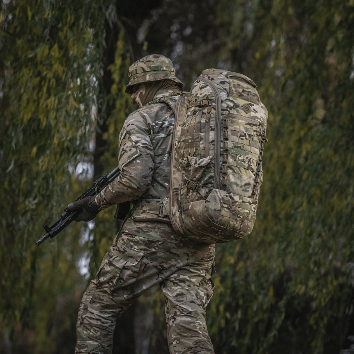 Sotilas metsäympäristössä kantaa maastokuvioitua M-Tac Large Gen.IV Elite -reppua.