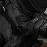 Henkilö pukeutuneena mustaan suojavarustukseen käyttää M-Tac Tourniquet Pouch Elastisk med MOLLE Gen.II:tä kiinnitettynä liiviin.