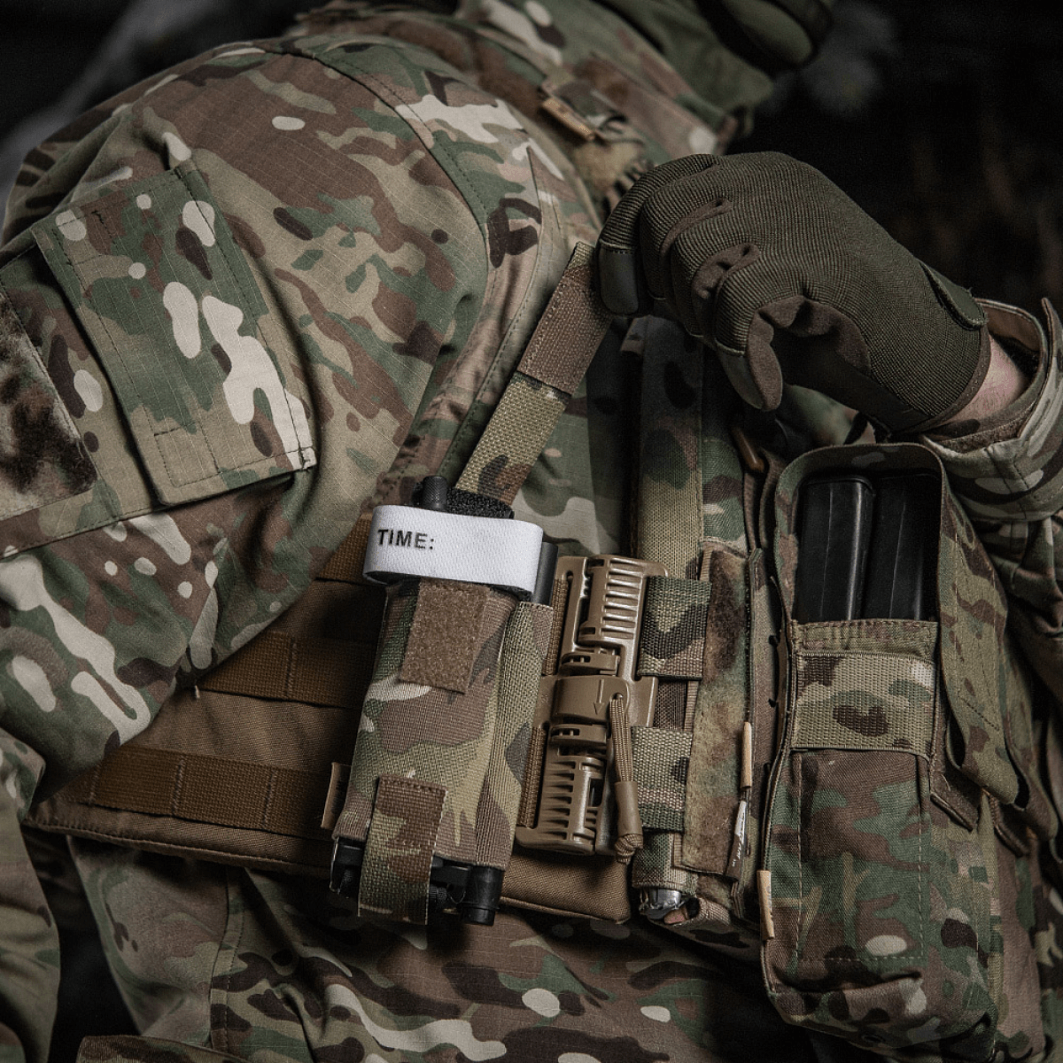 M-Tac Elastinen turnikekotelo Molle Gen.III kiinnitetty taktiseen liiviin tourniquetin ja lisävarusteiden kanssa sotilasalueella.