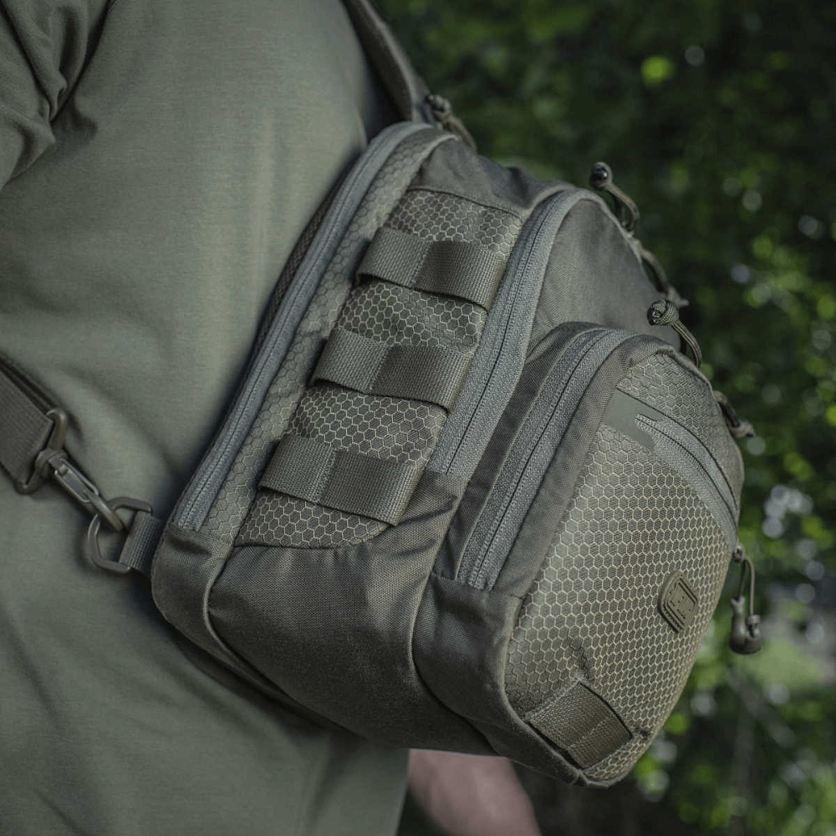 M‑Tac Cross Bag Elite Hex sling-laukku Cordura 500:sta, nähty olalla vihreässä ympäristössä, sopii päivittäiseen käyttöön ja taktisiin varusteisiin. 5 l.