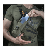 Mies, jolla on M-Tac Smartphone Lomme Elite Large Hex tummanvihreänä, pitää älypuhelinta kädessään.