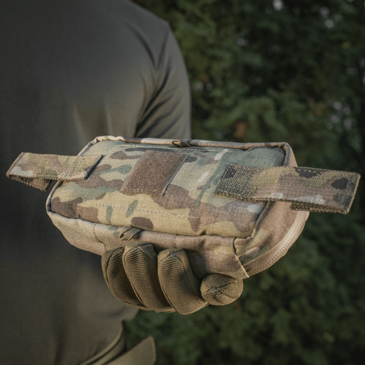 Henkilö pitää M‑Tac Horizontal Medical Pouch Eliteä maastokuvioisena, sopii kenttäkäyttöön ja ensiapuun, tukeva muotoilu ja vesitiivis vetoketju.