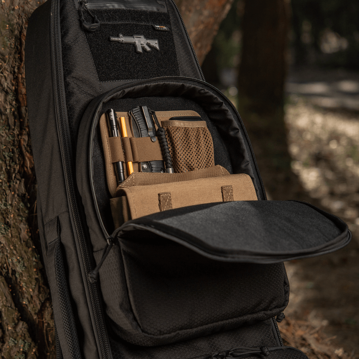 M‑Tac Gun Backpack Case 105 cm Elite Hex metsässä, avattuna osio varusteille.