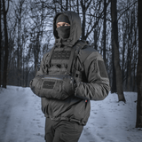 Henkilö käyttää M-Tac taktista käsilämmitintä Elite lumisessa metsässä, pitää kädet lämpiminä kylmässä säässä.
